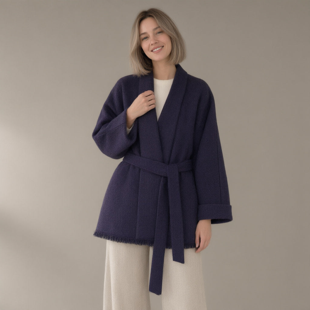 Woman wearing the belted wrap wool coat, fringed hem, three-quarter view, studio