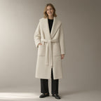 Woman wearing an ivory shawl-collar wrap coat belted over a black roll-neck, full length