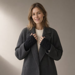 Woman in a charcoal wool coat wearing black cable-knit fingerless gloves, hands holding the lapels