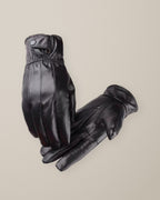 Women’s black goatskin leather gloves, fleece-lined, finger and back-of-hand seams, laid flat on a stone backdrop
